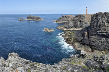 The lighthouse stands above a craggy headland.*